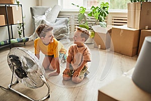 Two boys Sitting by Fan Indoors