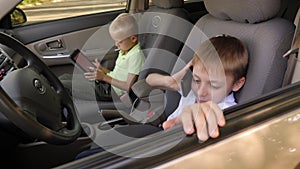 Two boys are sitting in the front seats of a car with a tablet and a phone.