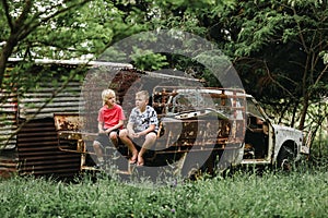 Two boys sitting on ruins of old truck on abandoned farm