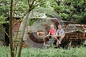 Two boys sitting on ruins of old truck on abandoned farm