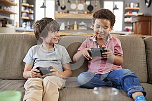 Two Boys Sitting On Sofa In Lounge Playing Video Game Together