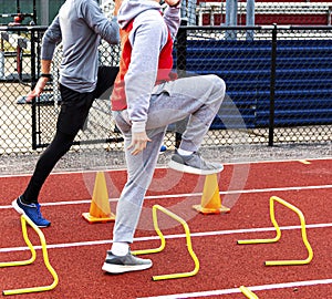 Two boys stepping over mini hurdles and orange cones on a track