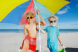 Two boys in sunglasses under parasol on a sand ocean beach