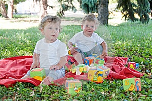 Two boys twins sitting on a red blanket with toys
