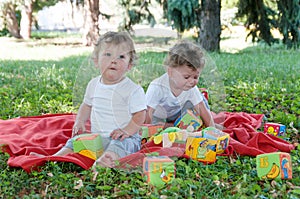 Two boys twins sitting on a red blanket with toys