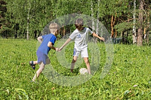 Two boys in uniform plays football on green meadow. Children run and kick soccer ball. Summer children outdoor games