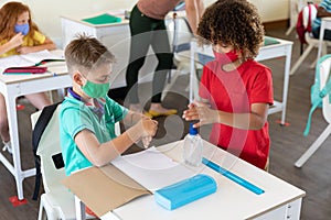 Two boys wearing face masks sanitizing their hands in class at school