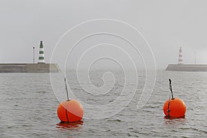 Two brant point lighthouses at harbor entrance in fog with two red bouys in the foreground