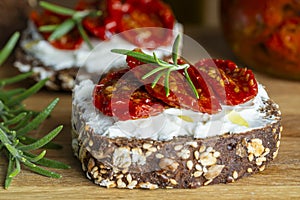 Two bread slices with ricotta cheese, olive and sun dried tomatoes on wooden board background. Delicious breakfast or wine snack.