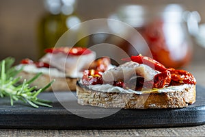 Two bread slices with ricotta cheese, pieces of herring and sun dried red tomatoes on wooden board background. Delicious breakfast