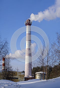 From two brick chimneys comes thick smoke. Smoke is clearly visible against the blue sky.