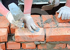 Two bricklayers are laying bricks of a brick wall, foundation using a mason`s trowel and mortar. A close-up of a brickwork from