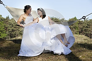 Two brides in hammock against blue sky with forest background