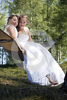 Two brides pose on hammock in forest on sunny summer day