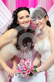 Two brides wearing white dresses hold bouquet