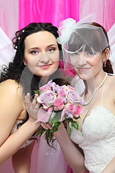 Two brides wearing white dresses hold bouquet