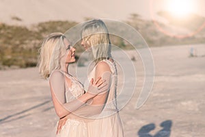Two brides women in white dress with blonde hair hugging each other