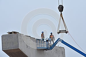 Two bridge construction workers wait on bridge parts