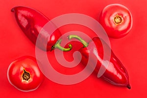 Two bright big red bell peppers and two red tomatoes on red background top view closeup