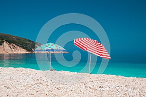 Two bright colored sun beach umbrella on pebble beach against turquoise blue sea water surface and clean blue sky