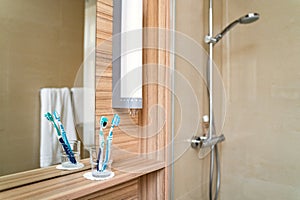 Two bright toothbrushes in glass cup in bathroom with mirror and shower cabin