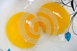 Two bright yellow yolk chicken eggs in a white bowl