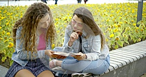 Two bright young girls who sit in the Park opposite the field with sunflowers, read one book for two