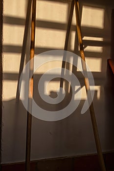 Two broomsticks against a wall with the shadow of a window