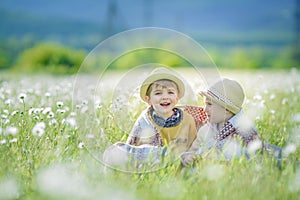 Two brothers children 6 years old in straw hats sitting together in the long grass in the meadow