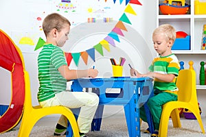 Two brothers draw pictures in the kids room.