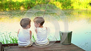 Two brothers fishing in the open air. Beautiful children have a good time in the summer on the lake.