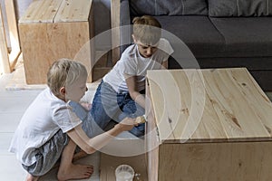 Two brothers help make the table. Joinery. Children paint wooden pedestal. Carpentry workshop