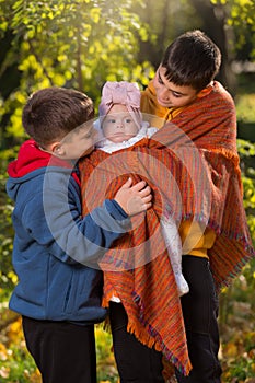 Two brothers hold their little sister in their arms - a baby, in nature, an autumn walk in the park