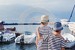 Two brothers hug and look at ships, yacht at sea