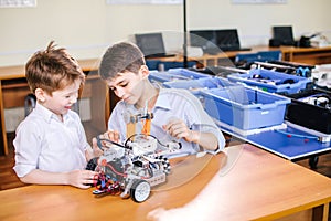 Two brothers kids playing with robot toy at school robotics class, indoor.