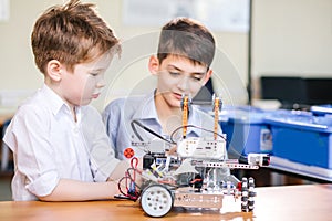 Two brothers kids playing with robot toy at school robotics class, indoor.