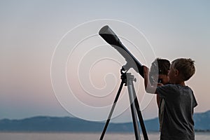 Two brothers looking at the stars using a telescope by the sea