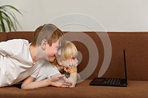 Two brothers lying on couch and stare at laptop monitor. Children watch cartoons