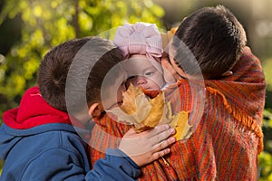 Two brothers - older and younger, in the autumn park, hold their sister - a baby, kissing her, close-up