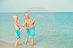 Two brothers play on the beach with water pistols. Summer time.