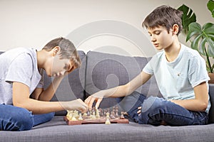 Two brothers are playing chess game while sitting on the couch. Strategic board game, leisure, entertainment at home