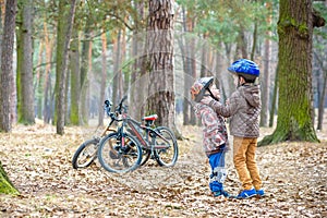 Two brothers preparing for bicycle riding in spring or autumn forest park. Older kid helping sibling to wear helmet. Safety and