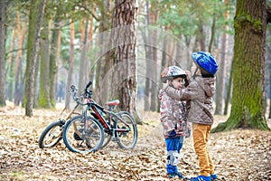 Two brothers preparing for bicycle riding in spring or autumn forest park. Older kid helping sibling to wear helmet. Safety and p