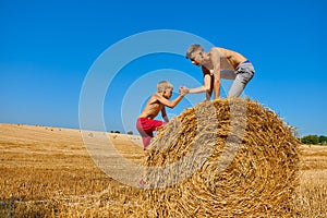 Two brothers push a haystack on an agricultural field. Summer scorching sun. Children`s day