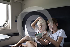 Two brothers ride in compartment carriage looking at phone. Entertaining children during trip. Travel by railway