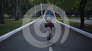 Two brothers riding a kick scooter in a summer park.