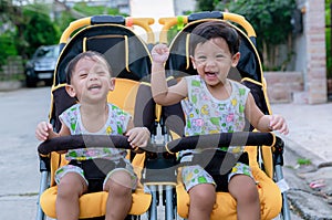 Two brothers sit in a stroller. Adorable twin baby boys sitting in stroller and smiling happily. Childhood emotions.