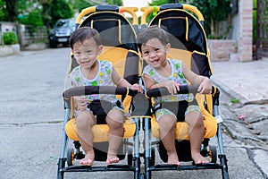 Two brothers sit in a stroller. Adorable twin baby boys sitting in stroller and smiling happily. Childhood emotions.