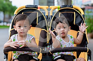 Two brothers sit in a stroller. Adorable twin baby boys sitting in stroller and smiling happily. Childhood emotions.