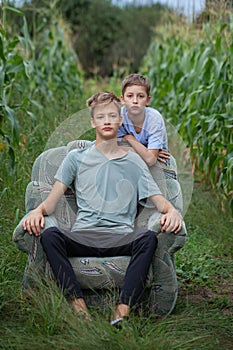 Two brothers sitting on a armchair in a field in the countryside in summer day